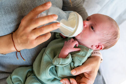 Ein Neugeborenes liegt bequem in den Armen einer anonymen Mutter und wird mit einer Milchflasche gefüttert, was einen nährenden und fürsorglichen Moment darstellt - ADSF54603