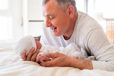 Ein liebenswerter Moment, in dem ein verspielter Vater mit seinem aufmerksamen neugeborenen Baby interagiert und beide eine herzliche Familienverbindung genießen - ADSF54607