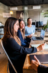 Three professional women actively engaged in a business meeting, reviewing content on a laptop. - ADSF54619