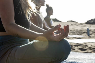 Women participate in a tranquil yoga class on the beach, performing meditation with the sun setting in the background. - ADSF54648