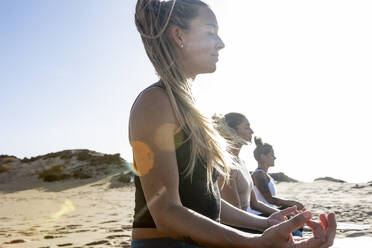 Women practice yoga in the peaceful evening ambiance of a beach setting, with gentle waves and the sunset providing a serene backdrop. - ADSF54649