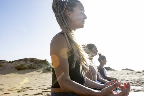 Die Frauen praktizieren Yoga in der friedlichen Abendstimmung eines Strandes, mit sanften Wellen und dem Sonnenuntergang als ruhiger Kulisse. - ADSF54649