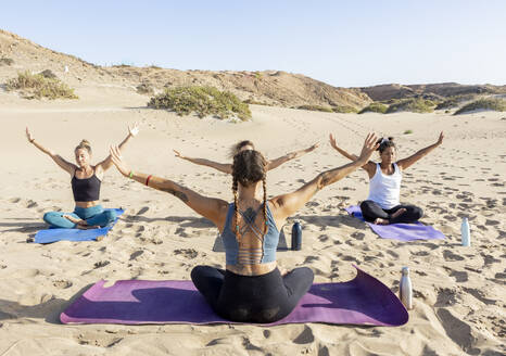 Women practice yoga poses on the beach during sunset, offering a tranquil and picturesque setting. - ADSF54651