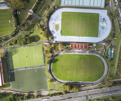Eine Drohnenaufnahme aus der Vogelperspektive, die verschiedene Sportplätze zeigt, darunter eine Laufbahn, ein Fußballfeld und Tennisplätze, umgeben von Grünflächen und städtischer Infrastruktur. - ADSF54664