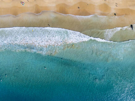 Eine Top-Down-Aufnahme von türkisfarbenen Wellen, die auf einen goldenen Sandstrand rollen, an dem Schwimmer und Sonnenanbeter die Schönheit der Küste genießen - ADSF54700