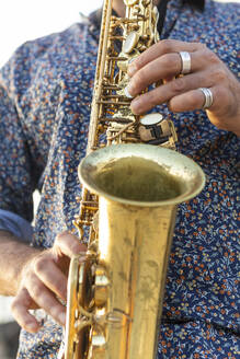 Ausschnitt eines männlichen Saxophonisten, der auf seinem Blechbläsersaxophon spielt und von der Kamera wegschaut, wobei Hände und Instrument im Mittelpunkt stehen. - ADSF54711