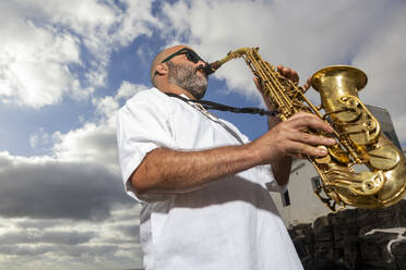 Von unten spielt ein Mann leidenschaftlich Saxophon im Freien, mit einem dramatischen Wolkenhimmel als Hintergrund, um den Geist des Internationalen Tages des Jazz zu feiern. - ADSF54715
