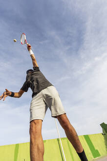 Niedriger Blickwinkel eines Mannes beim Tennisspielen, der den Ball vor dem Hintergrund des Himmels aufschlägt. - ADSF54719