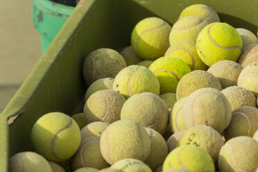 Eine Nahaufnahme von gebrauchten gelben Tennisbällen, die in einer grünen Tonne auf einem Tennisplatz gelagert werden. - ADSF54729