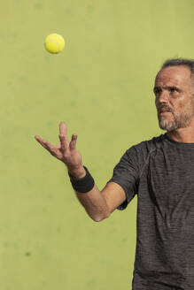 Ein reifer Mann mit konzentriertem Gesicht, der sich darauf vorbereitet, einen Tennisball in der Luft zu schlagen, vor einem grünen Hintergrund. - ADSF54732