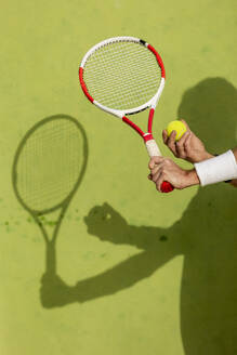 Ausgeschnittene, nicht erkennbare Hände, Schläger und Ball eines Tennisspielers, die einen Schatten auf den Platz werfen. - ADSF54735