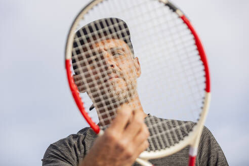 Ein unkenntlicher Mann hält sich einen Tennisschläger vor das Gesicht, wodurch seine Gesichtszüge teilweise verdeckt werden. - ADSF54737