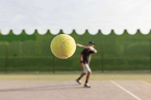 Tennisspieler, aufgenommen mitten in der Aktion während eines Rückhandschlags, Fokus auf den Tennisball mit dem Spieler im Hintergrund. - ADSF54740
