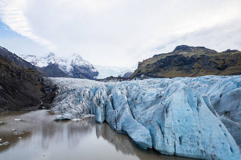 Der ausgedehnte Vatnajokull-Gletscher erstreckt sich in der Ferne, flankiert von Islands schroffen Bergen, die sich im ruhigen Gletscherwasser spiegeln - ADSF54751