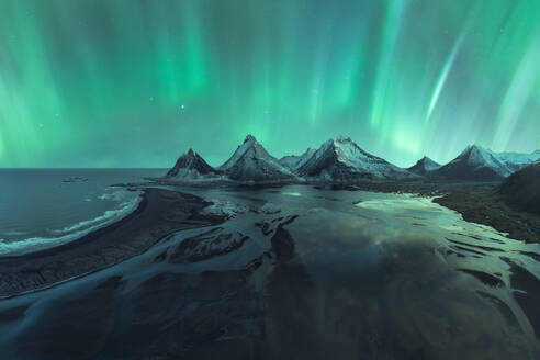 Ein atemberaubendes Schauspiel der Aurora Borealis, die den Nachthimmel über schneebedeckten Gipfeln und einer Küstenlandschaft in Island erleuchtet. - ADSF54754