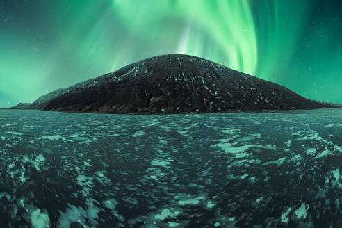 Ein spektakuläres Schauspiel der Aurora Borealis erhellt den Himmel über einer verschneiten, eisigen Landschaft in Island, mit einem Berg als Hintergrundkulisse. - ADSF54755