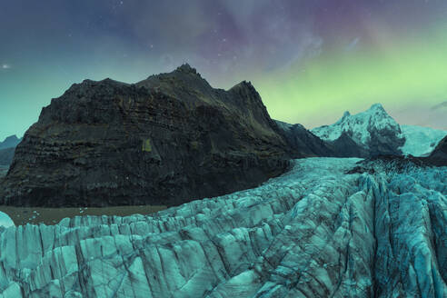 Nordlichter tanzen über der zerklüfteten Landschaft Islands und beleuchten die eisigen Gletscherformationen unter einem sternenklaren Himmel. - ADSF54758