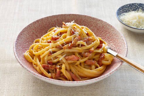 Ein Teller mit authentischen italienischen Spaghetti Carbonara, garniert mit geriebenem Käse und knusprigen Speckstücken. - ADSF54770