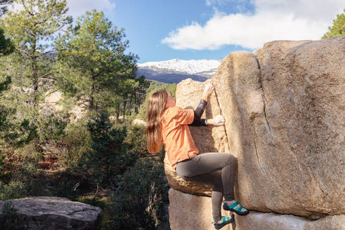 A lone climber skillfully ascends a tall boulder, with a stunning snow-capped mountain range in the distance - ADSF54777