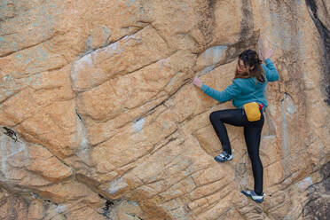 Eine konzentrierte Kletterin mit einem Chalkbag manövriert strategisch an einer steilen Felswand während einer Outdoor-Klettertour - ADSF54780