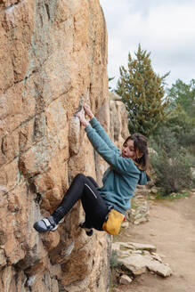 Eine junge Kletterin mit einem Chalkbag hält sich konzentriert an einer steilen Felswand fest und zeigt ihr Können beim Bouldern - ADSF54781