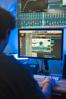 Abgeschnittener, nicht erkennbarer Produzent, der in einem Aufnahmestudio arbeitet und sich auf Audio-Mixing-Software auf Computerbildschirmen konzentriert. - ADSF54801