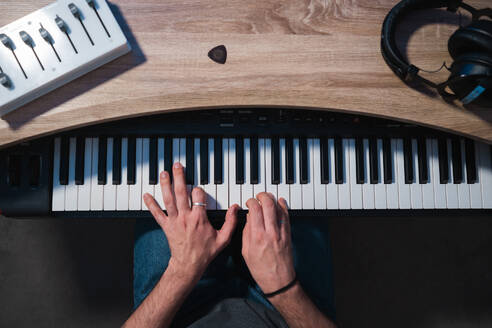 Von oben abgeschnittene, nicht erkennbare Musikerhände, die anmutig ein elektronisches Keyboard während einer Tonstudiositzung spielen, mit Tonmischer und Kopfhörern in der Nähe. - ADSF54809