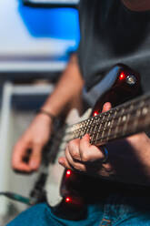 Abgeschnittene, nicht erkennbare Hände eines männlichen Musikers, der während einer Aufnahmesitzung eine E-Gitarre spielt, mit Studioausrüstung im Hintergrund. - ADSF54813