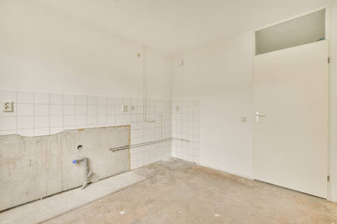 Ein leerer Raum mit weiß gefliesten Wänden, die Anzeichen von Verfall aufweisen, und Räumen, aus denen Einrichtungsgegenstände entfernt wurden. - ADSF54845
