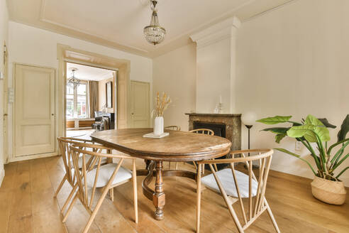 Ein gemütliches und stilvolles Esszimmer mit einem runden Holztisch im Vintage-Stil, weißen gepolsterten Stühlen und einem klassischen Kronleuchter. - ADSF54847