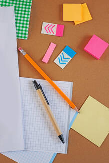 Draufsicht auf Büromaterialien wie Haftnotizen, Millimeterpapier und Bleistifte auf einer braunen Oberfläche, die ein ordentliches und organisiertes Arbeitsplatzkonzept darstellt. - ADSF54853