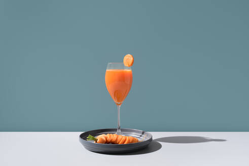 An exquisite arrangement featuring a refreshing cocktail garnished with a slice of citrus and smoked salmon delicately placed on a sleek black plate, casting soft shadows on a minimalist surface. - ADSF54863