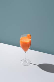 Ein erfrischendes Glas mit Orangensaft, garniert mit einer Scheibe, die einen Schatten auf eine weiße Fläche wirft. - ADSF54867