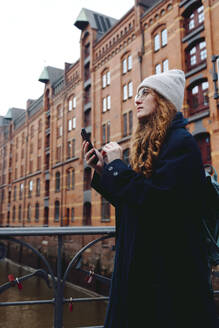 A red haired female tourist wandering through Hamburgs Speicherstadt, checking her phone and enjoying the view. - DANF00051