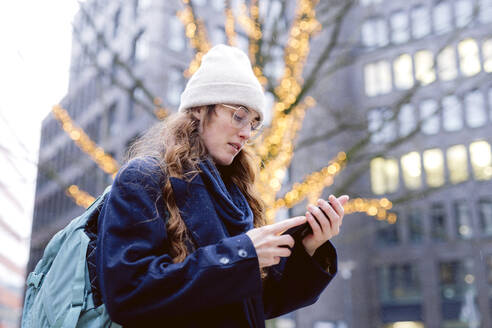 A red haired woman using her phone and taking pictures next to a Christmas light like decorated tree close to the city center in Hamburg, Germany. - DANF00083