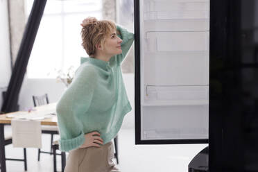 Ukraine, woman in blue sweater opens a black refrigerator at light kitchen interior - ONAF00762