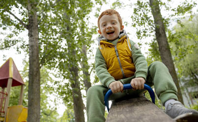 A cheerful red-haired boy is swinging on a swing in the playground. - MBLF00320