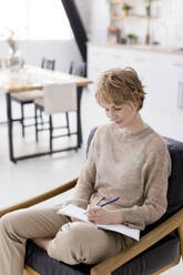 Ukraine, a woman sits on a chair and writes in a notebook at light interior - ONAF00772