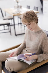 Ukraine, a woman sits on a chair and writes in a notebook at light interior - ONAF00775