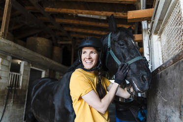 Lächelnder Trainer mit schwarzem Pferd im Stall - NDEF01620