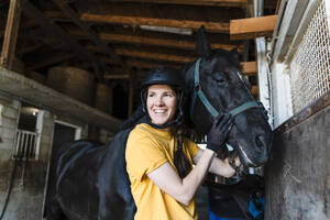 Smiling trainer with black horse in stable - NDEF01620