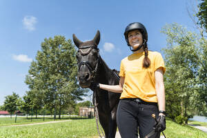 Happy trainer walking with black horse on sunny day - NDEF01642