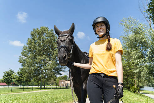 Glücklicher Trainer, der mit einem schwarzen Pferd an einem sonnigen Tag spazieren geht - NDEF01642