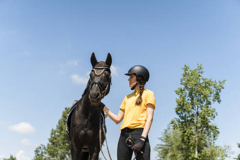 Trainer mit Helm und schwarzem Pferd an einem sonnigen Tag - NDEF01643