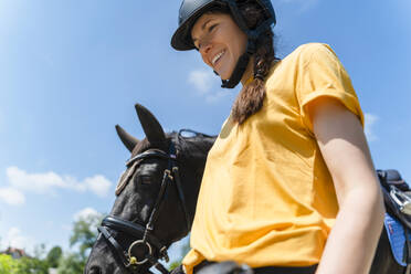 Lächelnder Trainer mit Helm, der mit seinem Pferd an einem sonnigen Tag spazieren geht - NDEF01644