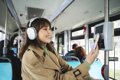 Glückliche Frau kauft Fahrkarte im Bus über ihr Smartphone - ALKF01125