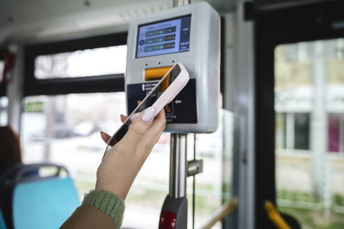 Hand einer Frau, die über ihr Smartphone eine Fahrkarte im Bus kauft - ALKF01126