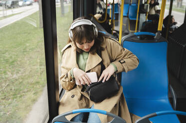 Junge Passagierin hält Smartphone und sucht in der Handtasche - ALKF01134