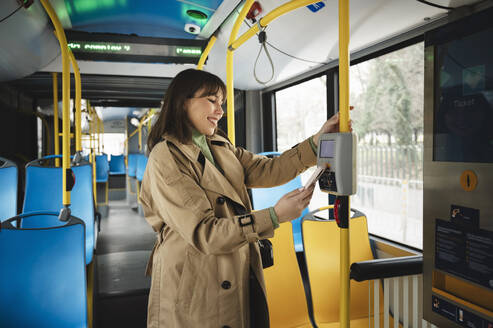 Zufriedener Fahrgast beim Kauf einer Fahrkarte im Bus durch kontaktloses Bezahlen mit dem Smartphone - ALKF01140