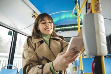 Lächelnder Fahrgast kauft Fahrkarte im Bus durch kontaktloses Bezahlen mit dem Smartphone - ALKF01141